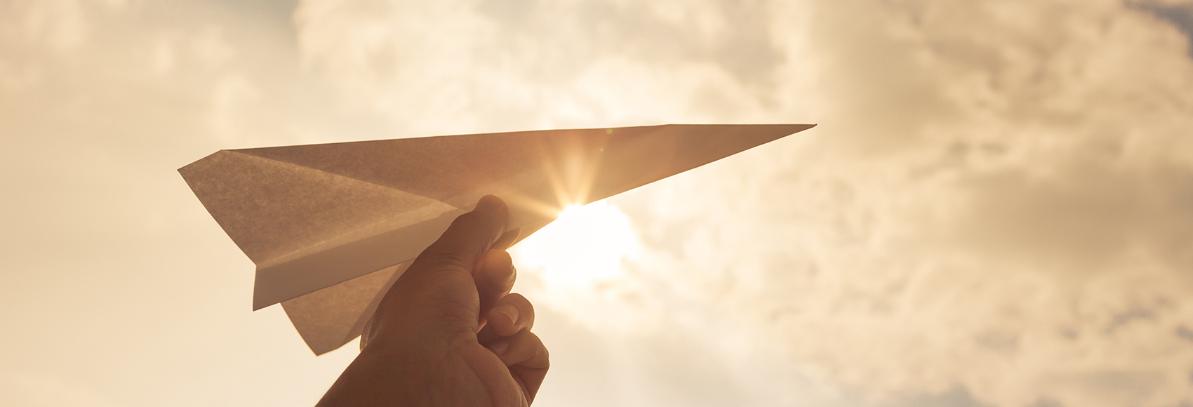 Hand holding paper airplane in the sky.